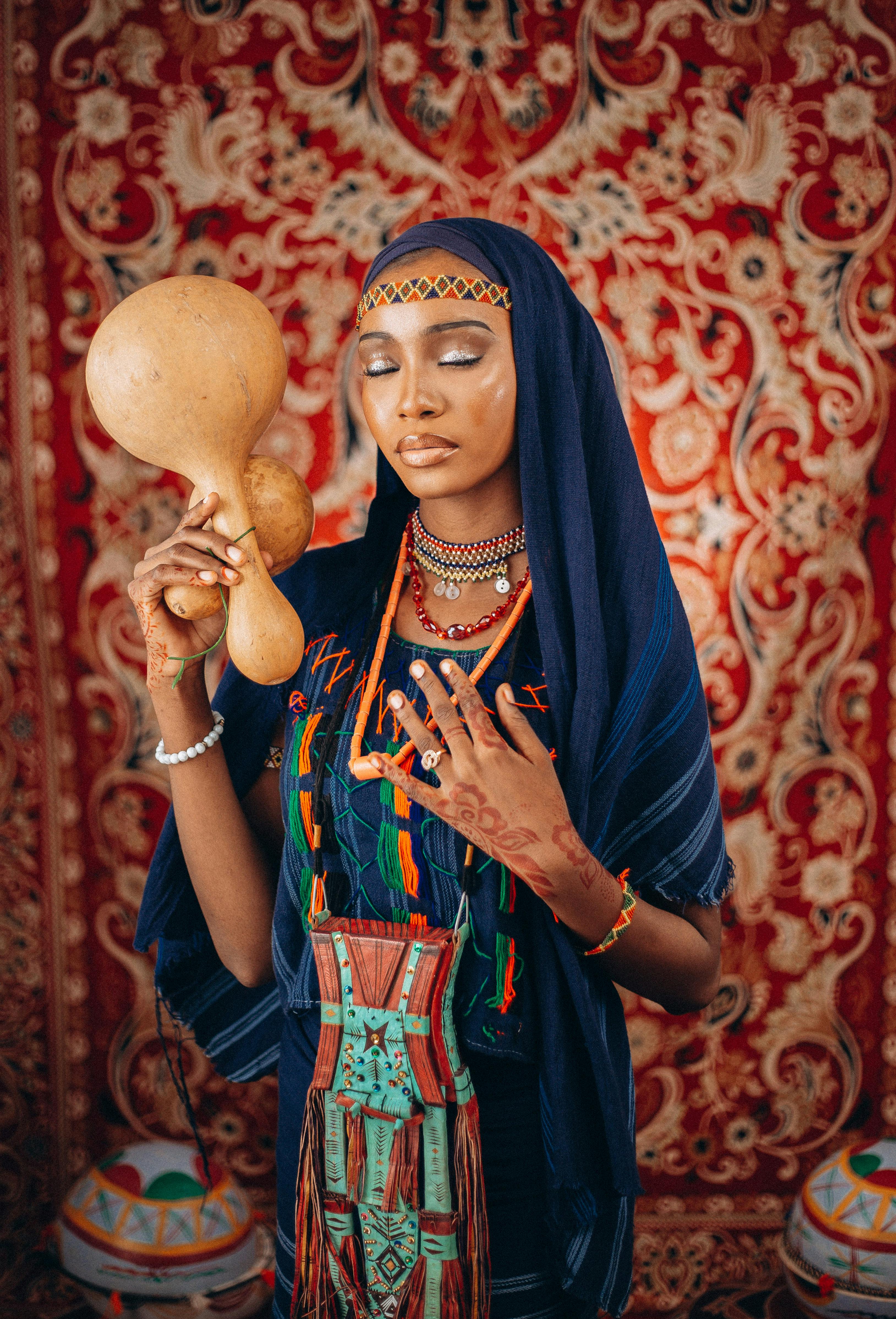 Beautiful woman in traditional attire holding gourds against ornate background.