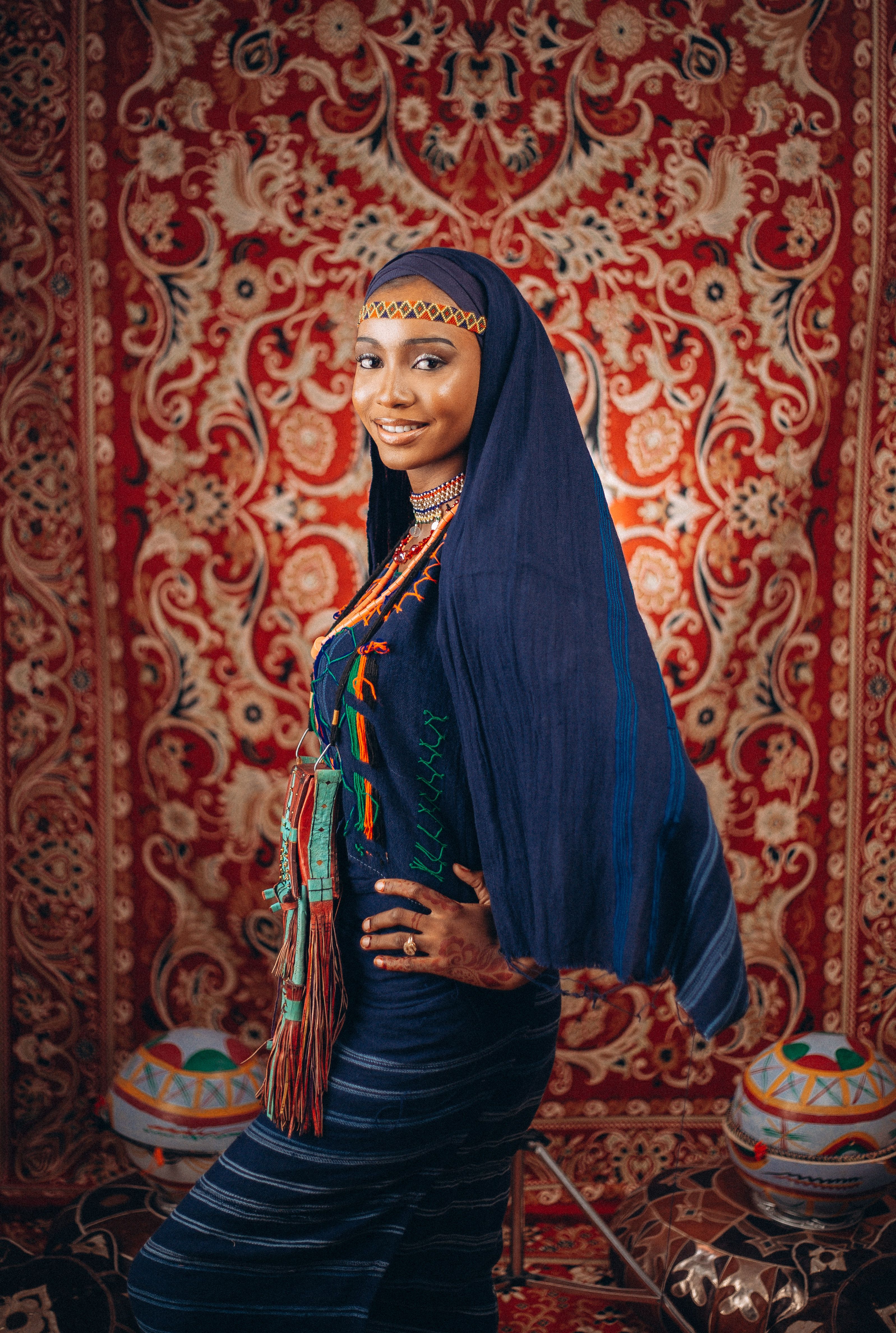Woman in ornate traditional African clothing with colorful background.