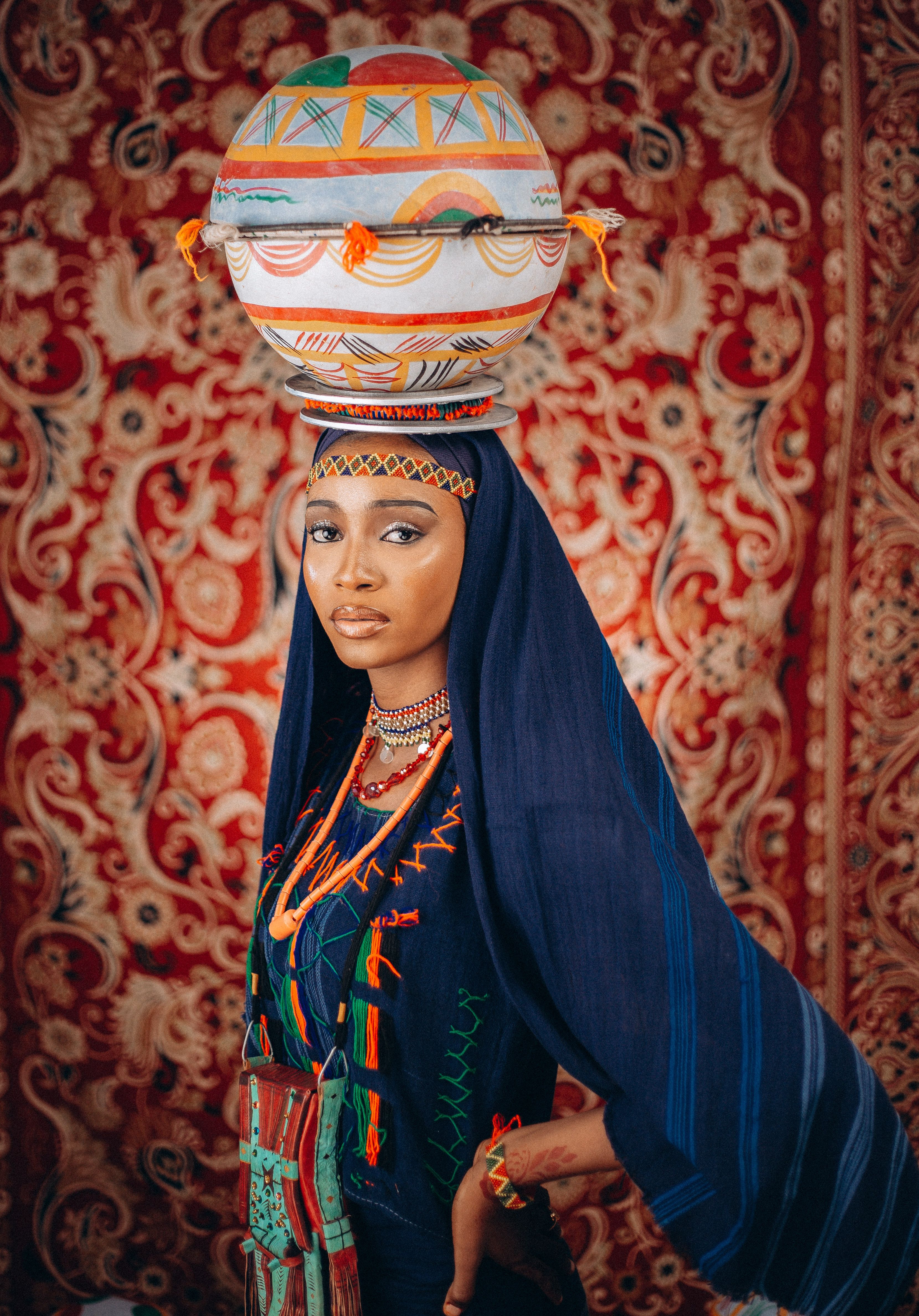 Elegant African woman in traditional attire with decorative vessel, vivid cultural portrait.