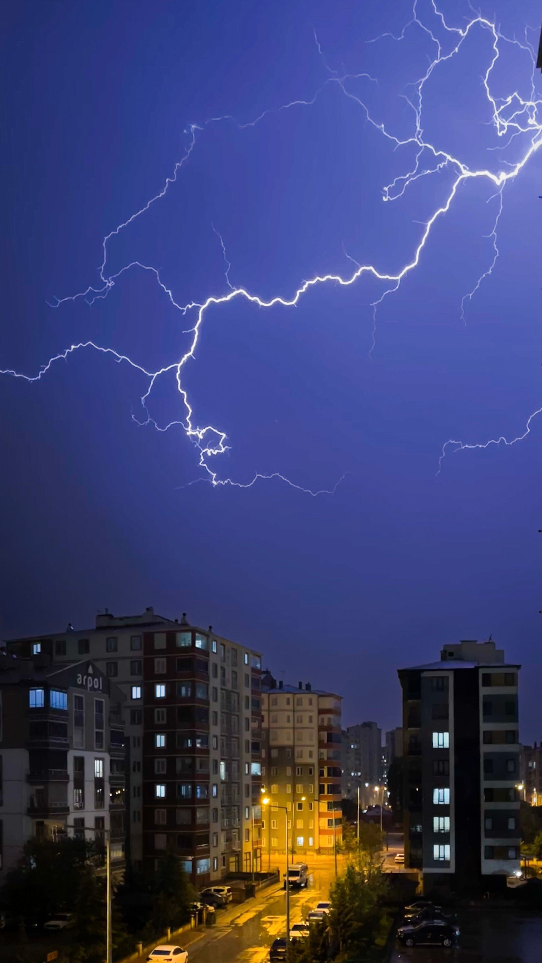 Striking lightning illuminates urban night sky above city buildings.