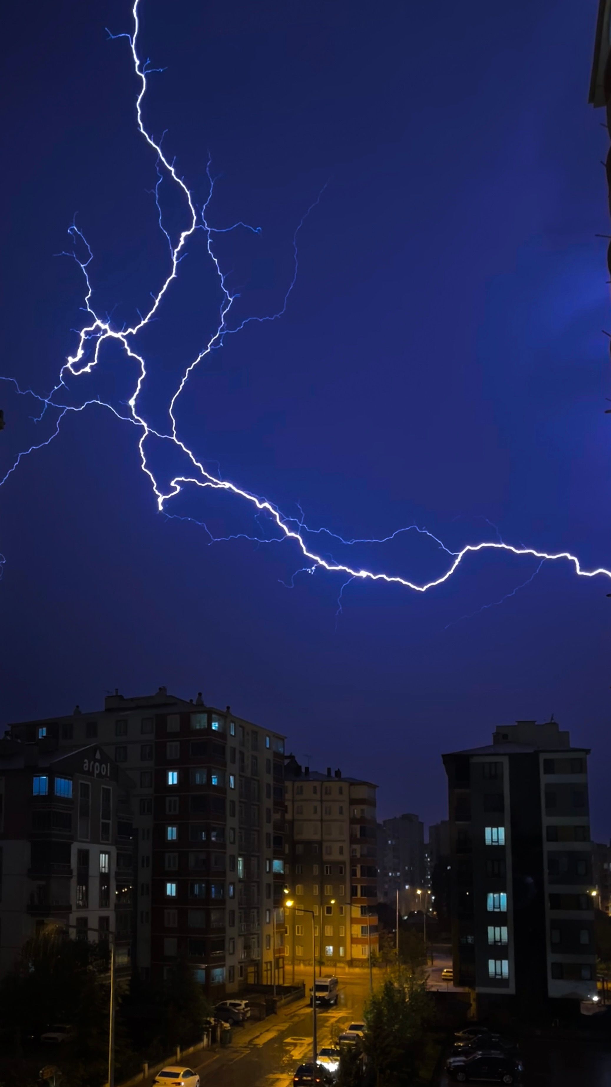 Striking lightning bolt over urban buildings at night, illuminating the sky.