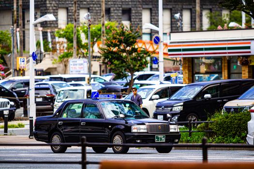 A bustling street with a black taxi and background of parked cars and a convenience store.