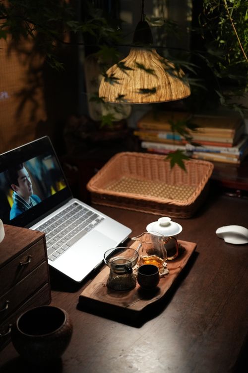 Free A warm indoor workspace featuring a laptop, a wooden tea set, soft lighting, and decorative plants. Stock Photo