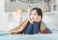 一位轻松的女人在节日的卧室里，穿着舒适的毛衣，盖着毯子