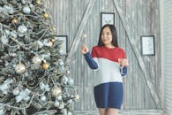 一位喜庆的女子手持烟火和一杯葡萄酒，站在室内装饰的圣诞树旁