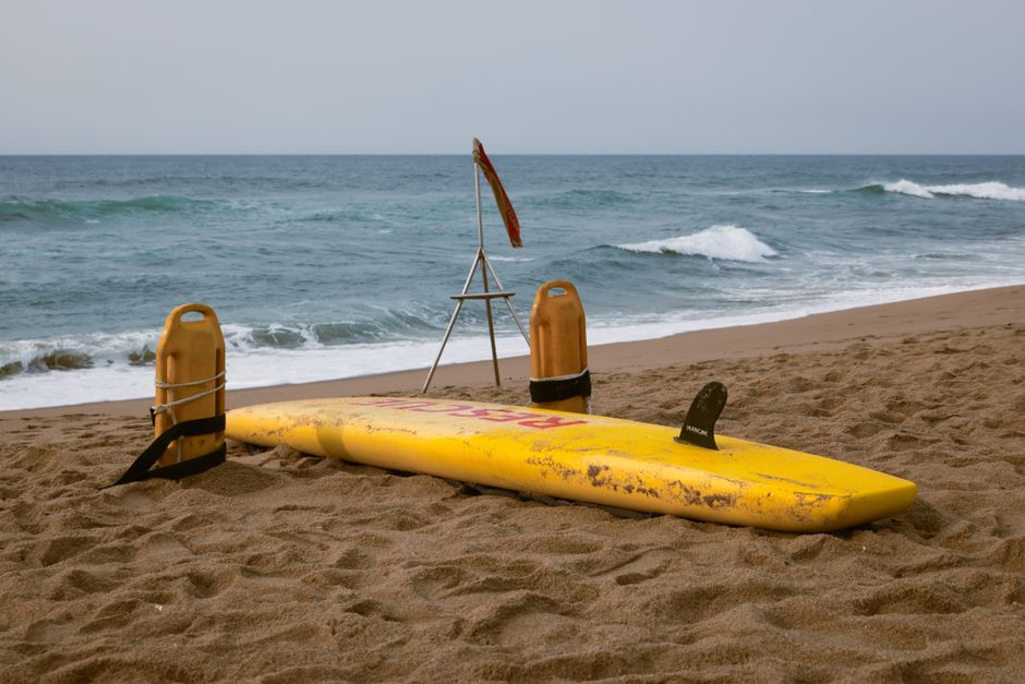 Surfboard and rescue buoys on a beach, ready for lifeguard duty by the ocean waves.