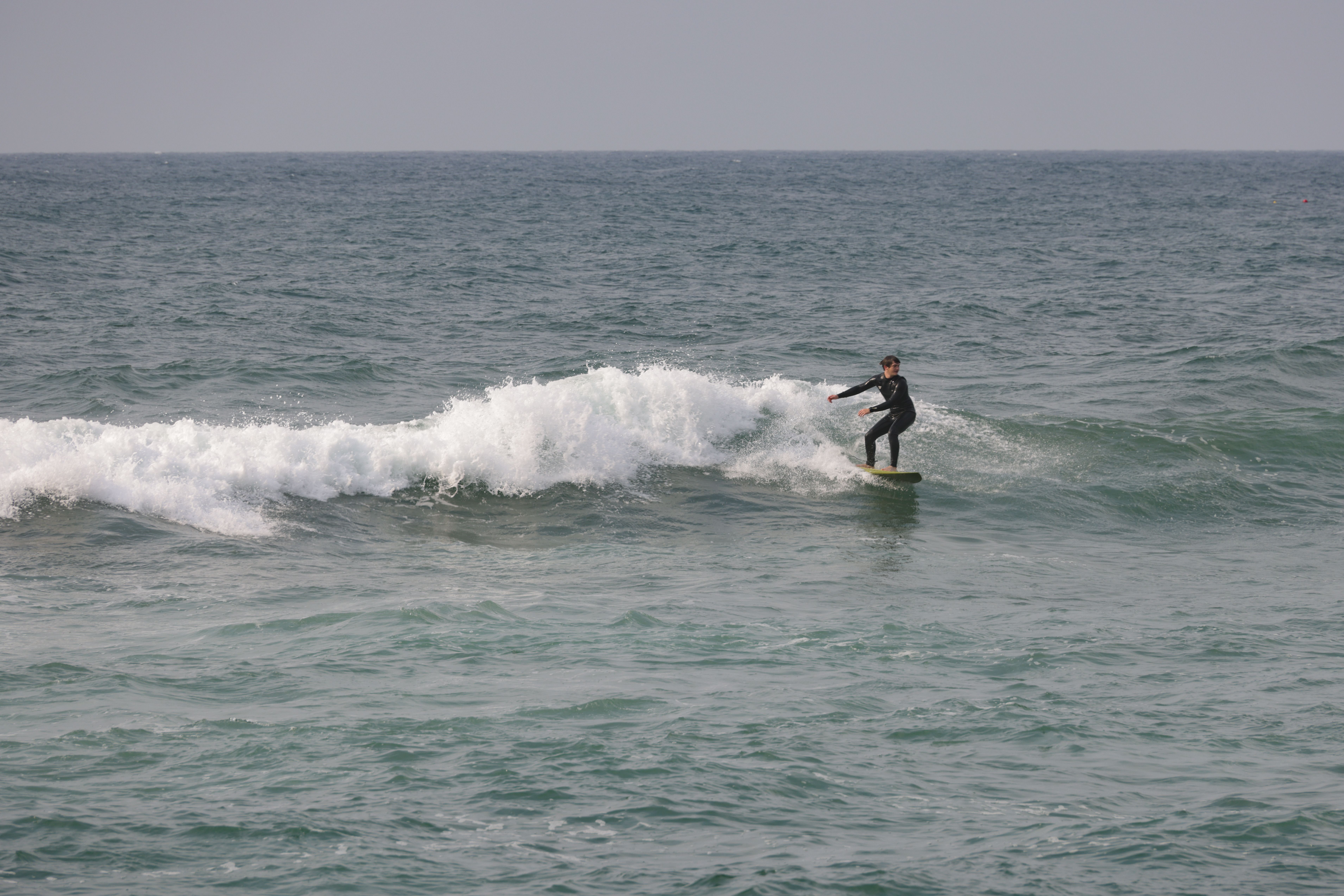 A lone surfer skillfully rides a wave on a sunny beach day.