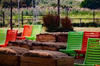 Bright green and red plastic chairs arranged in an outdoor garden with sunlight and greenery.
