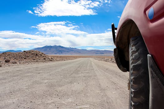 Close-up of an off-road vehicle tire on a vast desert road with mountains in the background.