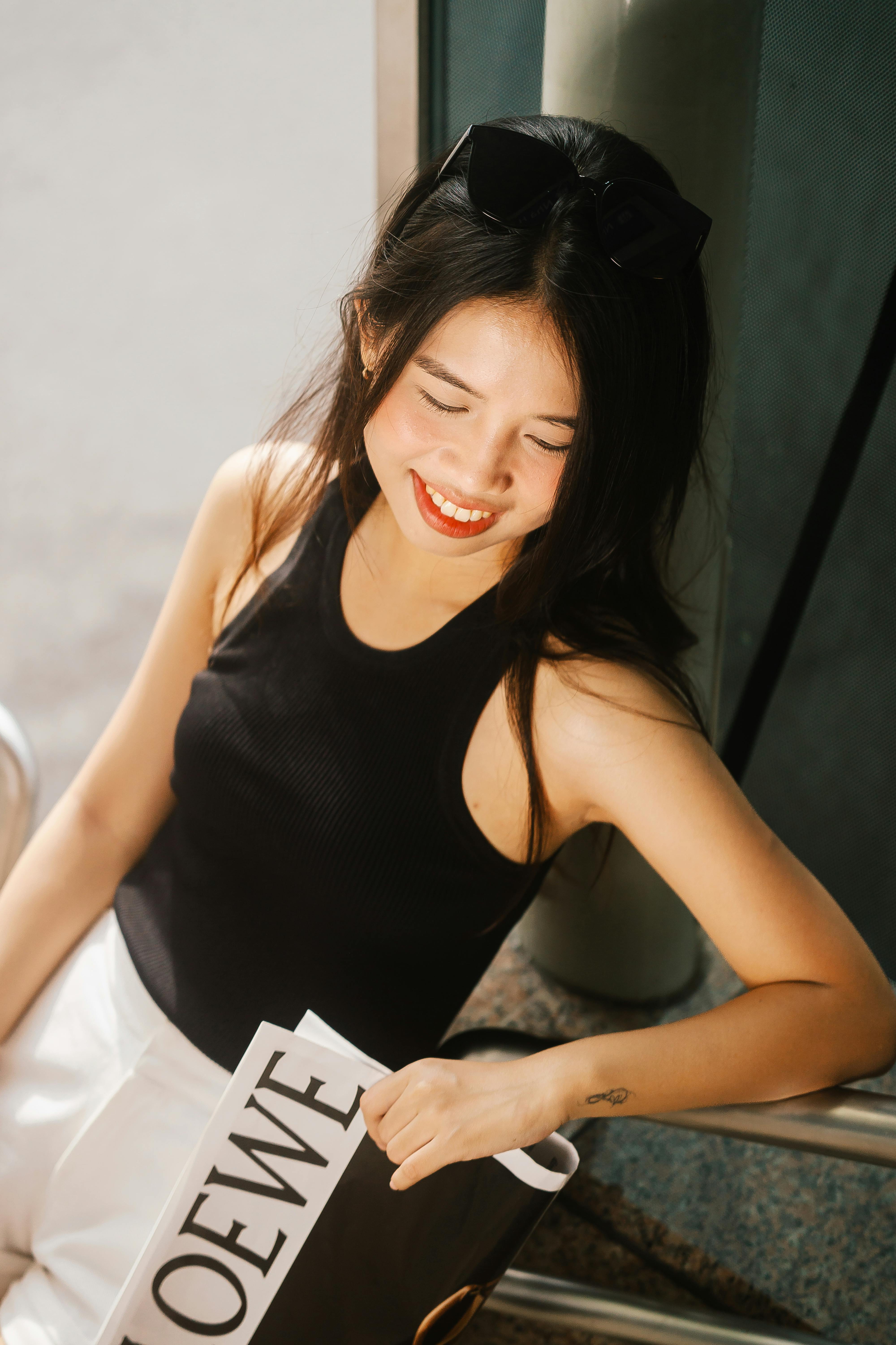 A smiling young woman in summer attire enjoys sunny outdoor weather.