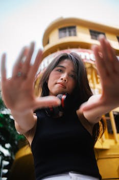 Young woman wearing headphones poses confidently in front of urban architecture.