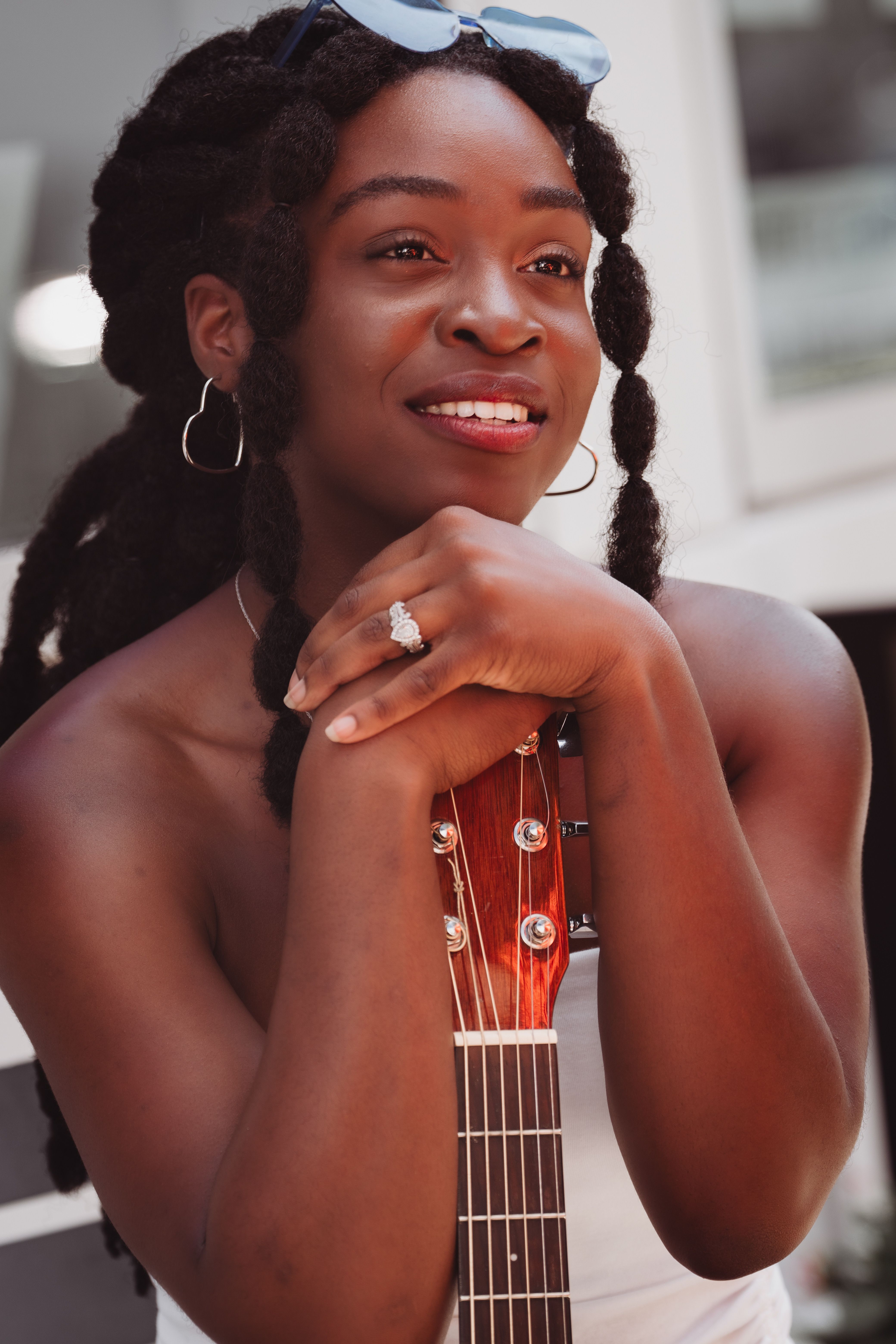 Confident woman with dreadlocks holding a guitar and smiling outdoors.