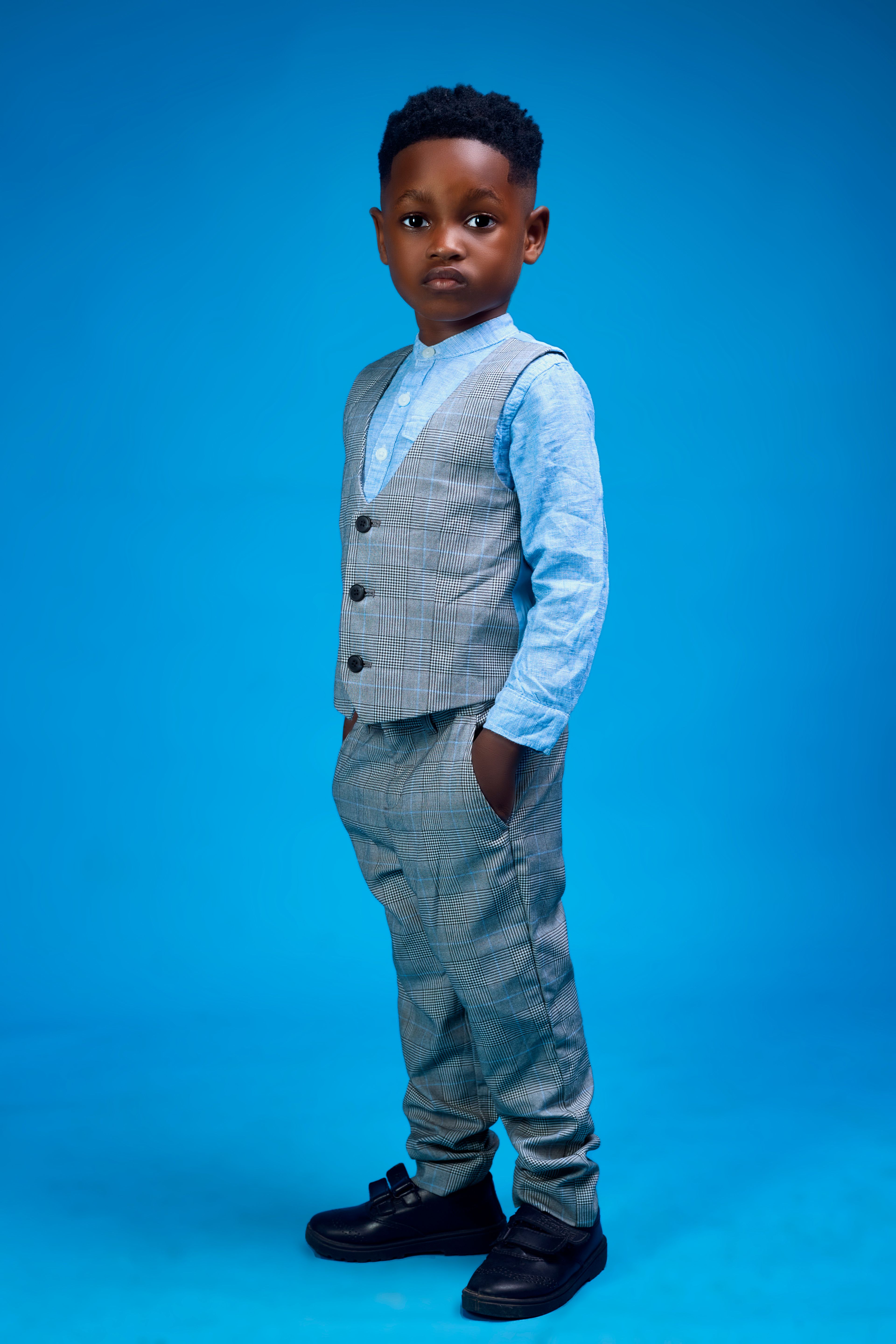 Young boy poses confidently in a stylish suit against a vibrant blue backdrop.