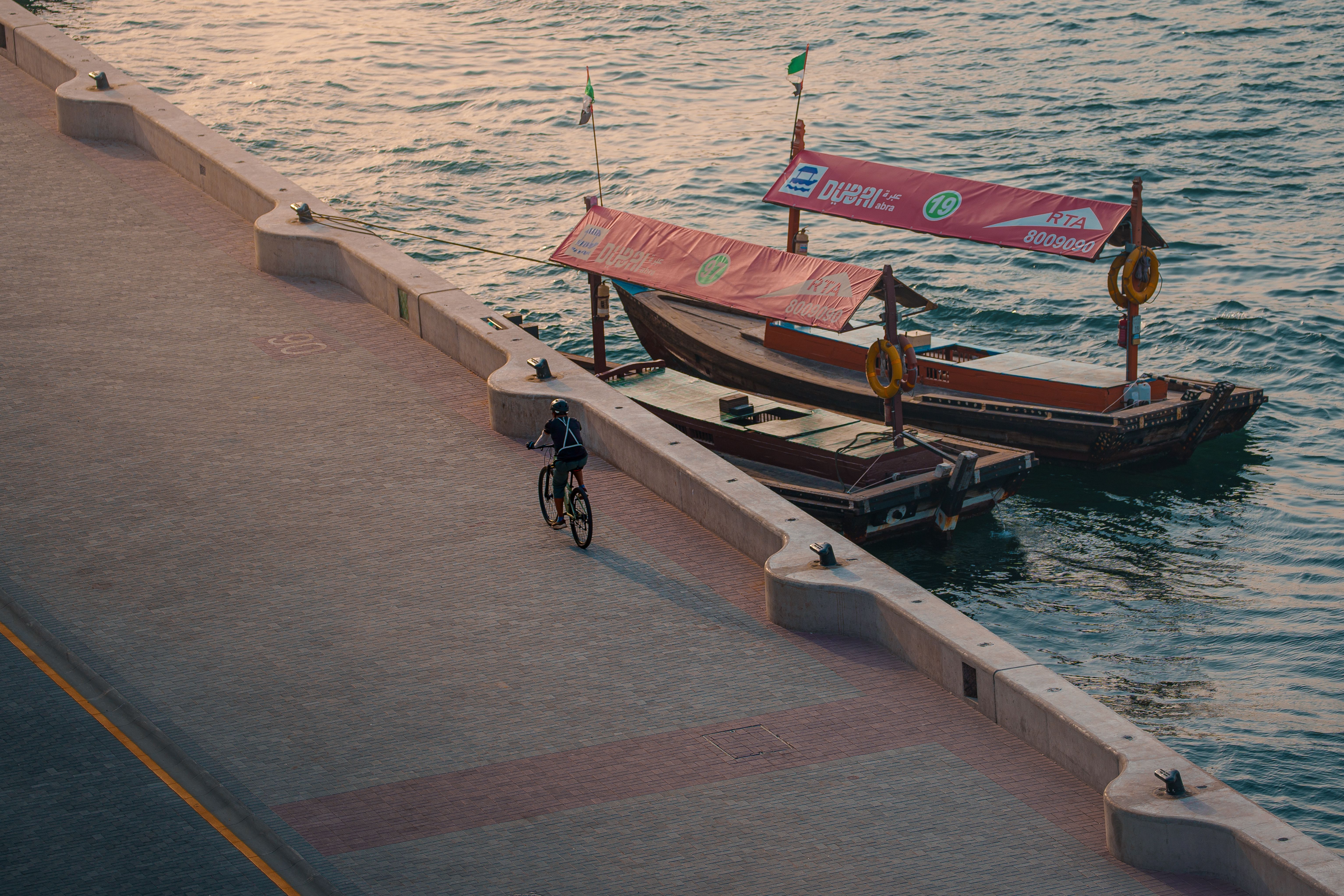 Aerial view of a cyclist riding along the Dubai waterfront with traditional boats in the background