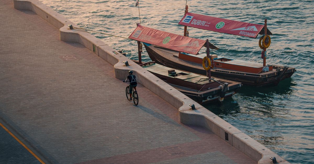 Aerial view of a cyclist riding along the Dubai waterfront with traditional boats in the background
