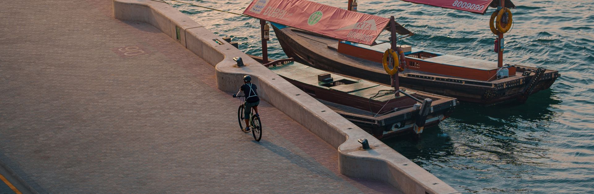 Aerial view of a cyclist riding along the Dubai waterfront with traditional boats in the background