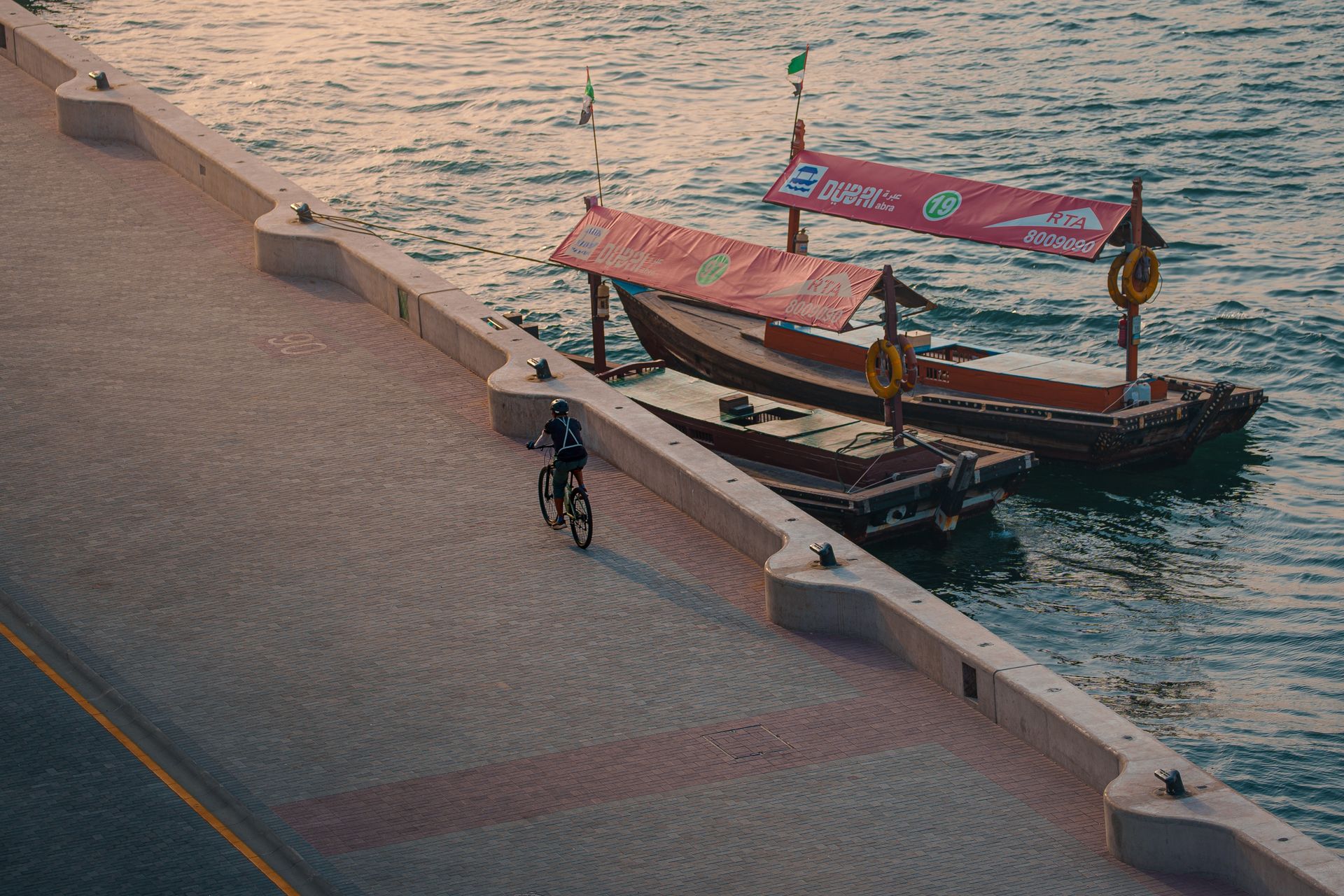 Aerial view of a cyclist riding along the Dubai waterfront with traditional boats in the background
