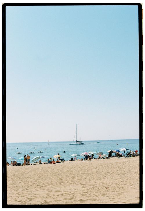 Free Crowded beach with colorful umbrellas and a sailboat on the horizon. Stock Photo