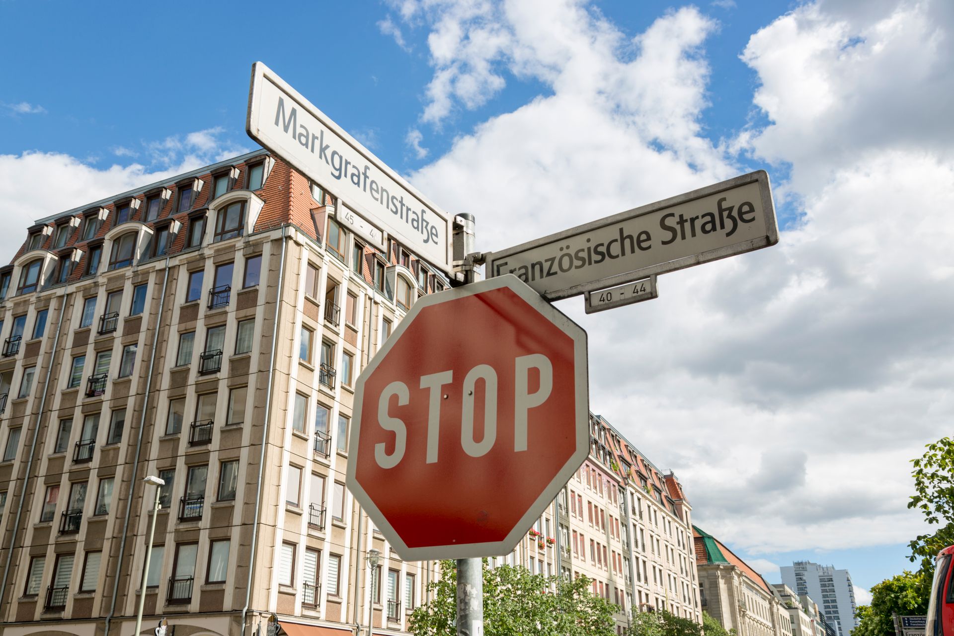 Street signs and stop sign near historic European architecture under a partly cloudy sky.