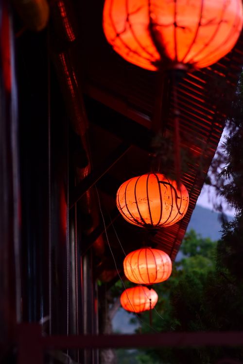 Free A row of illuminated red lanterns hanging from a sloped roof, creating a warm glow against a night sky. Stock Photo