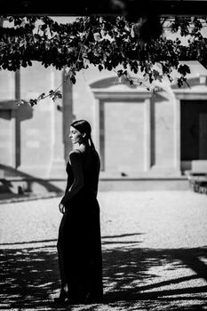 Black and white image of a woman posing outdoors in an elegant dress, capturing a stylish mood.