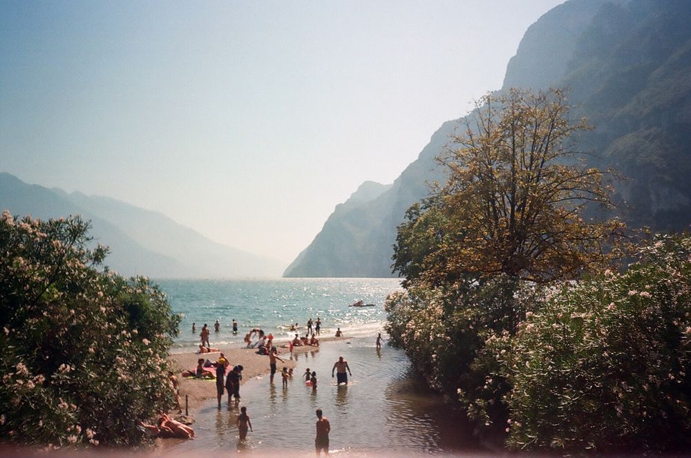 Plajă pe Lacul Garda cu oameni la scăldat și munți în fundal