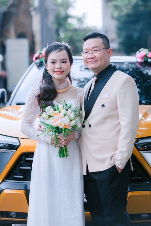 Free Bride and groom smiling in front of a yellow car adorned with flowers. Stock Photo