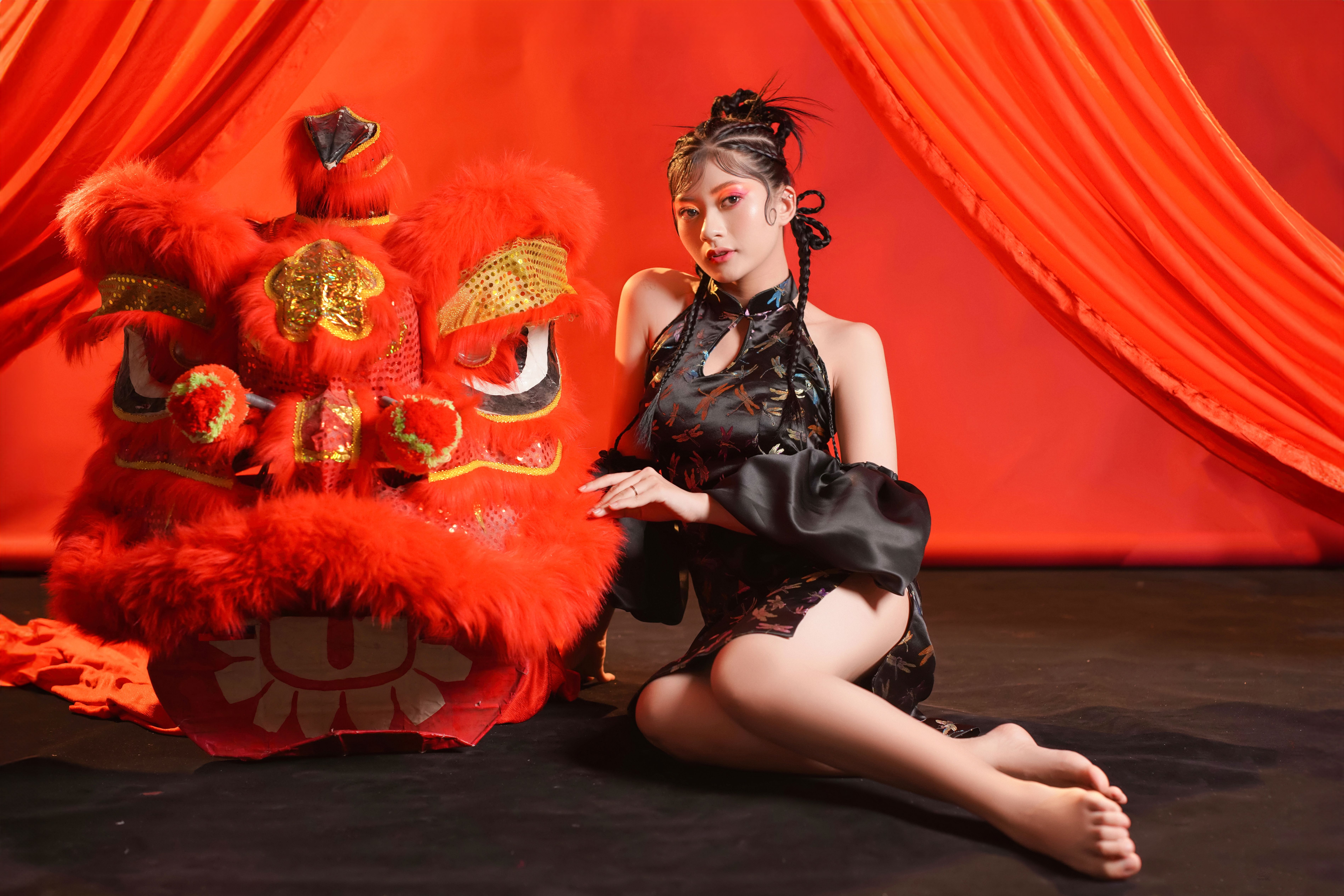 Femme asiatique assise à côté d'un costume de danse du dragon vibrant, orné de rideaux rouges.