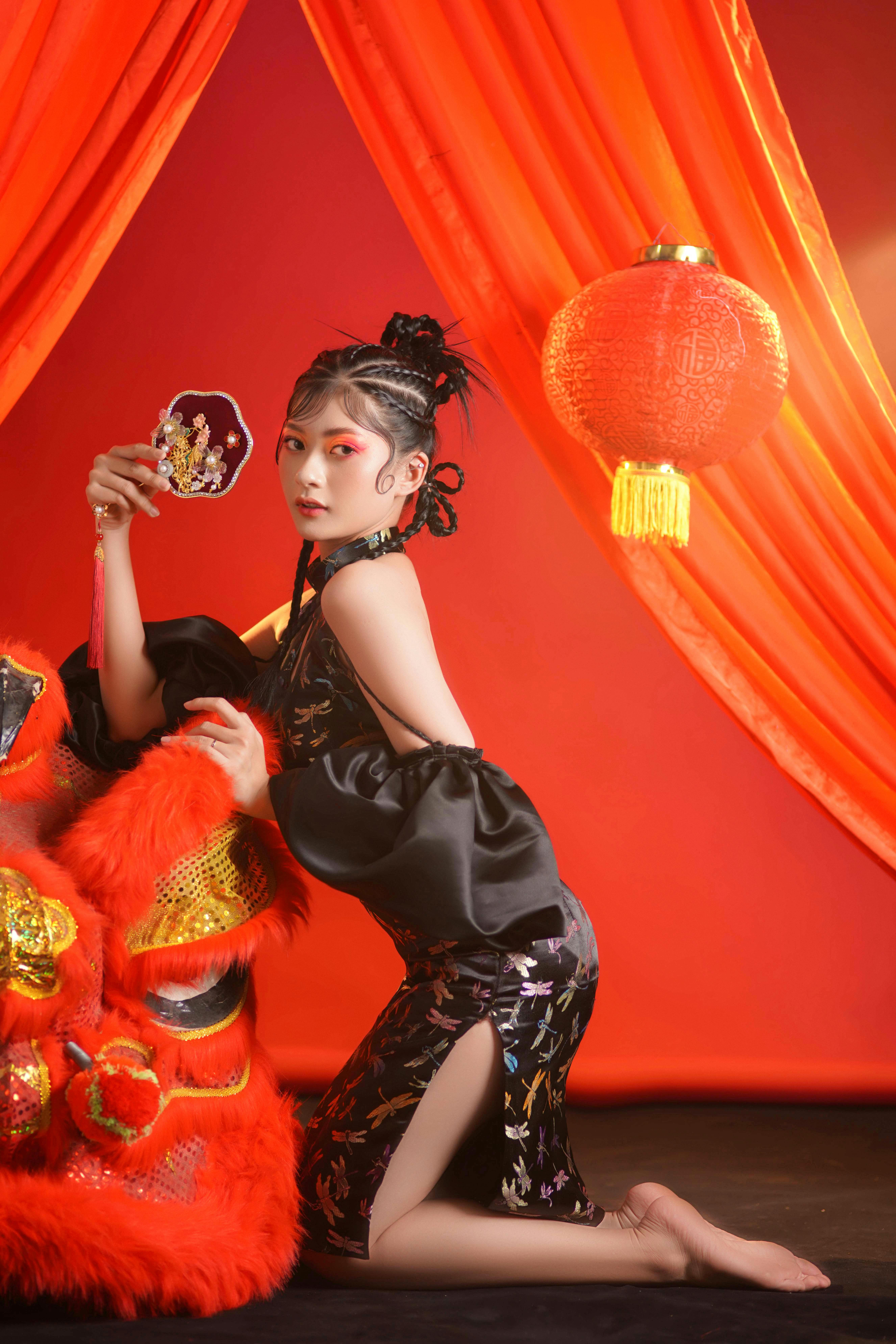 Graceful woman in traditional attire with lantern and vibrant red backdrop, embodying East Asian culture.