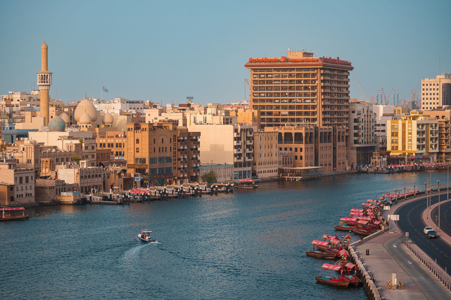 A beautiful view of Dubai Creek showcasing traditional buildings and abra boats in warm daylight.