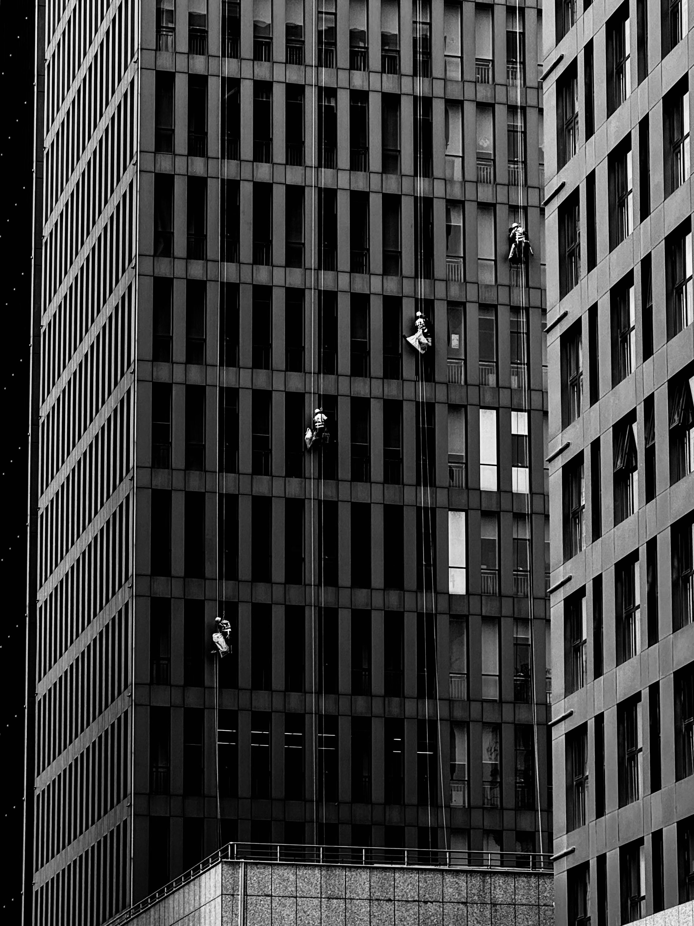 Daring window washers cleaning skyscraper windows at night, silhouetted against a city backdrop.