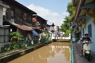 A vibrant street along a canal with a scooter rider in Asia, showcasing local life.