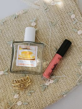 Elegant flat lay of Crème Caramel perfume, lip gloss, and hair clip on woven background.