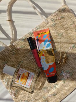 Flat lay of cosmetics and accessories on a straw bag in natural light.
