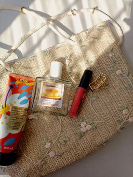 Stylish flat lay of cosmetic products on an embroidered bag in soft sunlight.