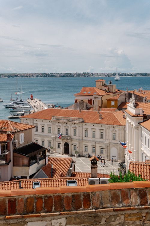 Free A picturesque view of a Slovenian coastal town with red rooftops and serene sea under a blue sky. Stock Photo