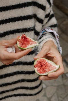 Close-up of hands holding cut figs against a background of a striped sweater in Piran, Slovenia.