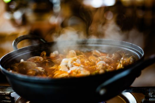 Delicious seafood stew bubbling in a black pot with steam rising indoors.