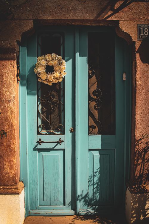 Free Discover the beauty of a rustic blue door adorned with a white floral wreath, bathed in warm sunlight. Stock Photo