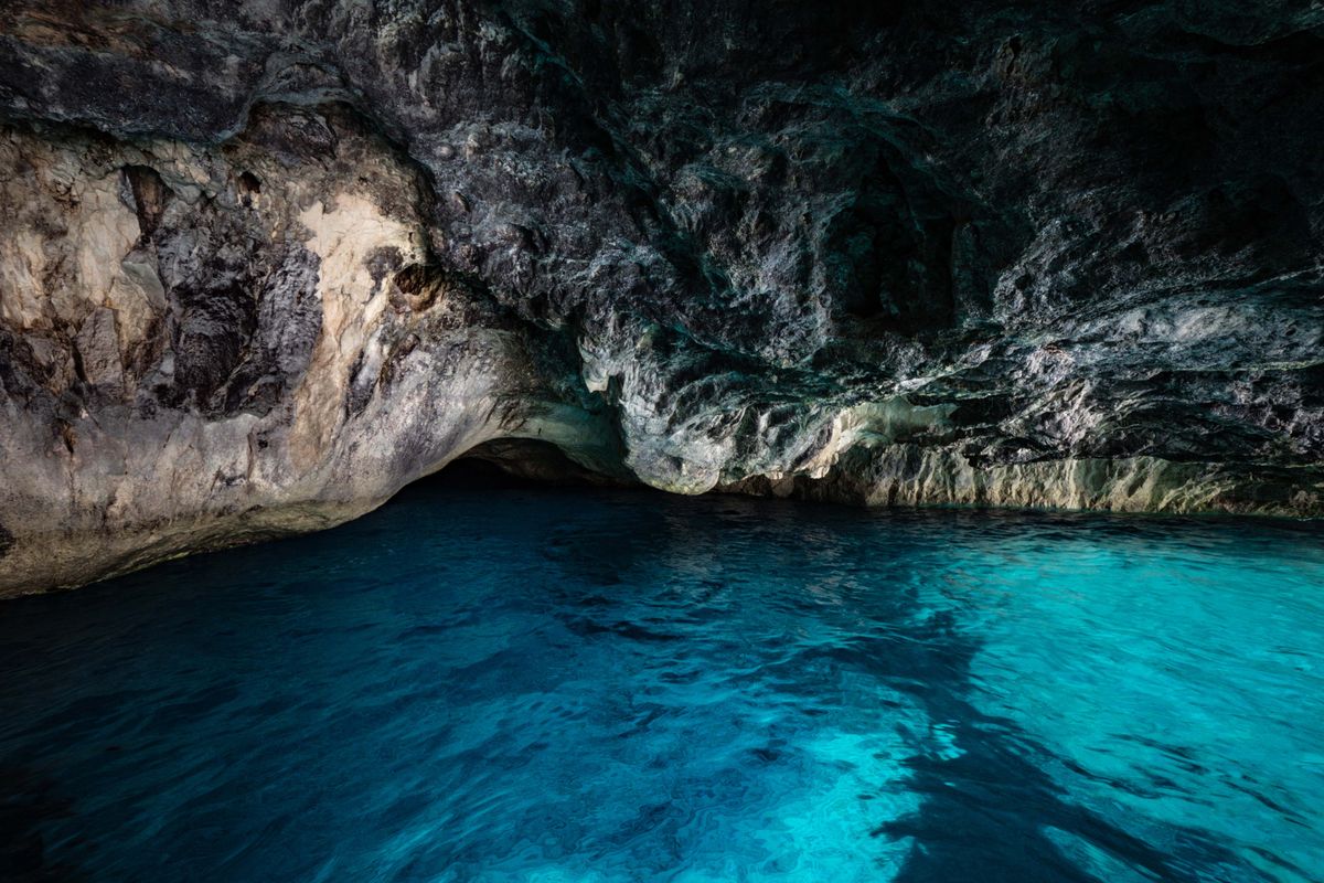 The interior of a limestone sea cave with dark rock overhead and clear turquoise water below