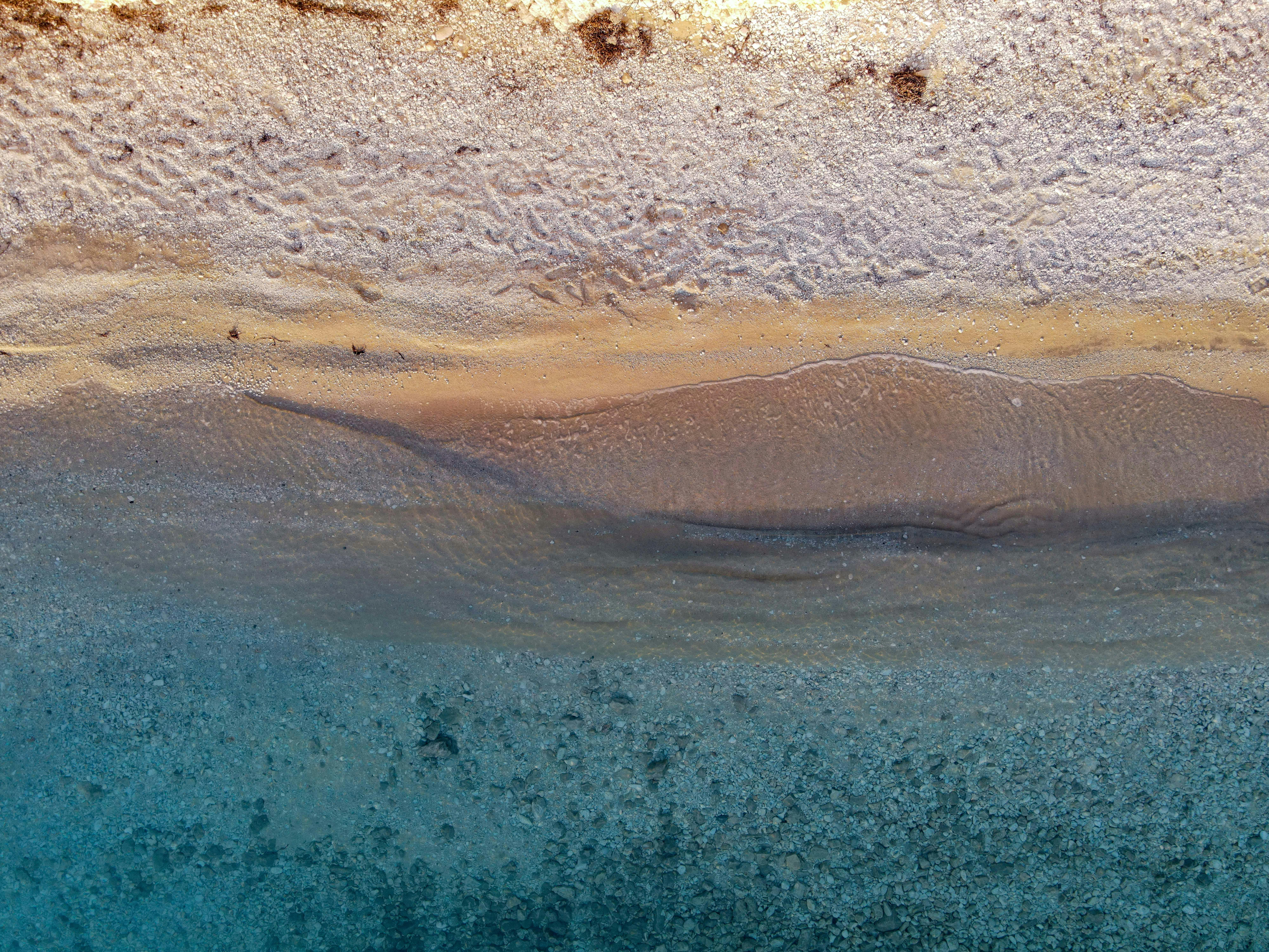 Stunning aerial view of a tranquil beach shoreline highlighting sand patterns and vibrant water hues.