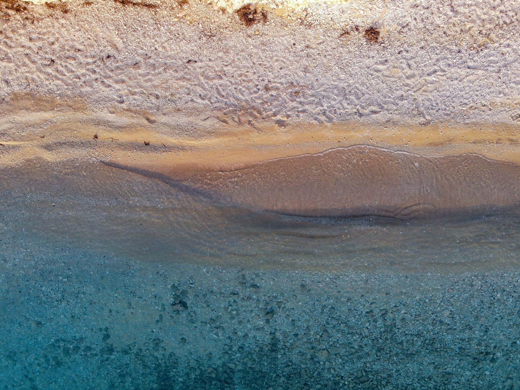 Stunning aerial view of a tranquil beach shoreline highlighting sand patterns and vibrant water hues.