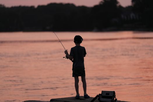 A young boy engaging in fishing at sunrise on a tranquil morning in Cove Island Park, Stamford, Connecticut.
