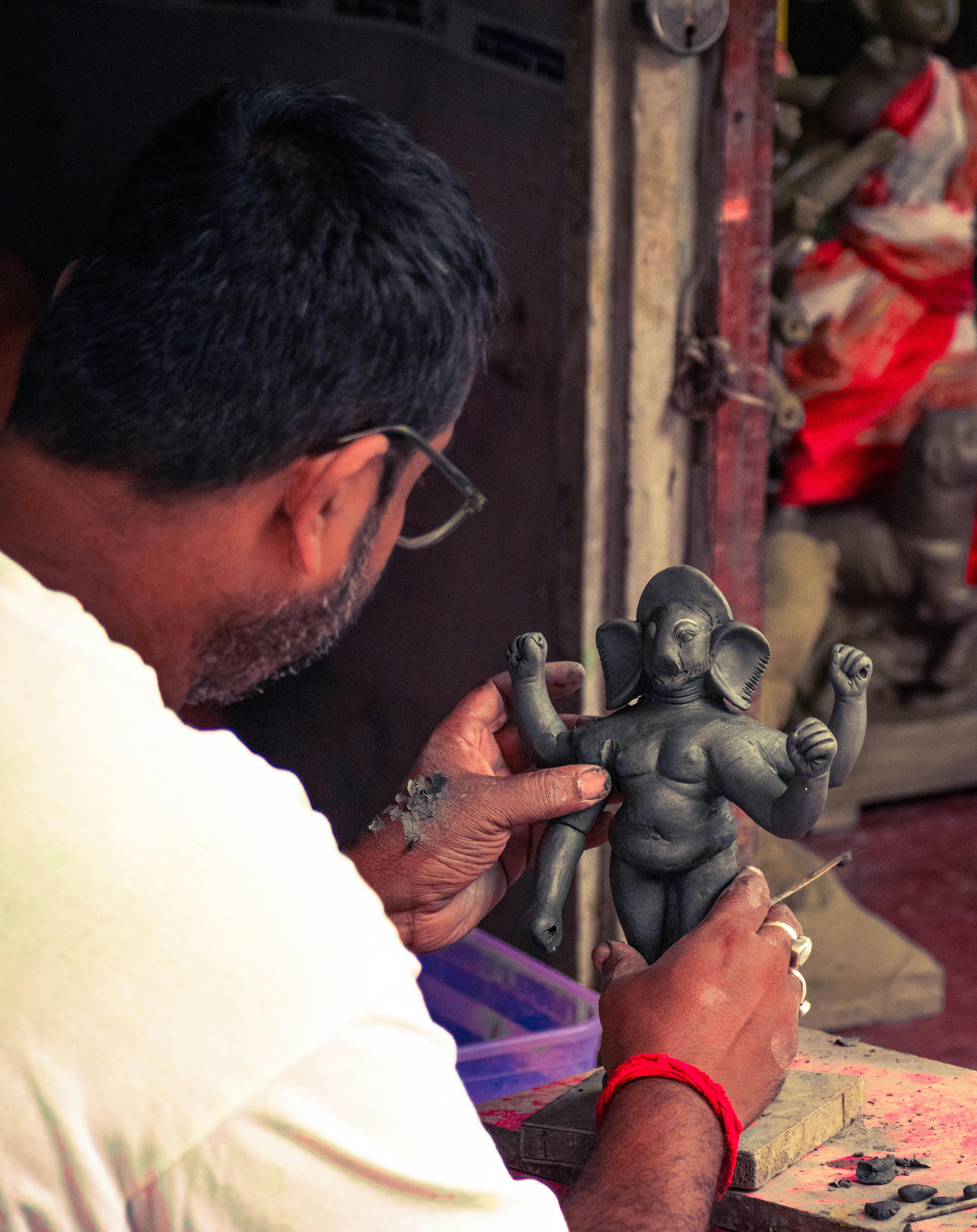 Artisan skillfully molds a clay Ganesh statue, showcasing traditional craftsmanship.