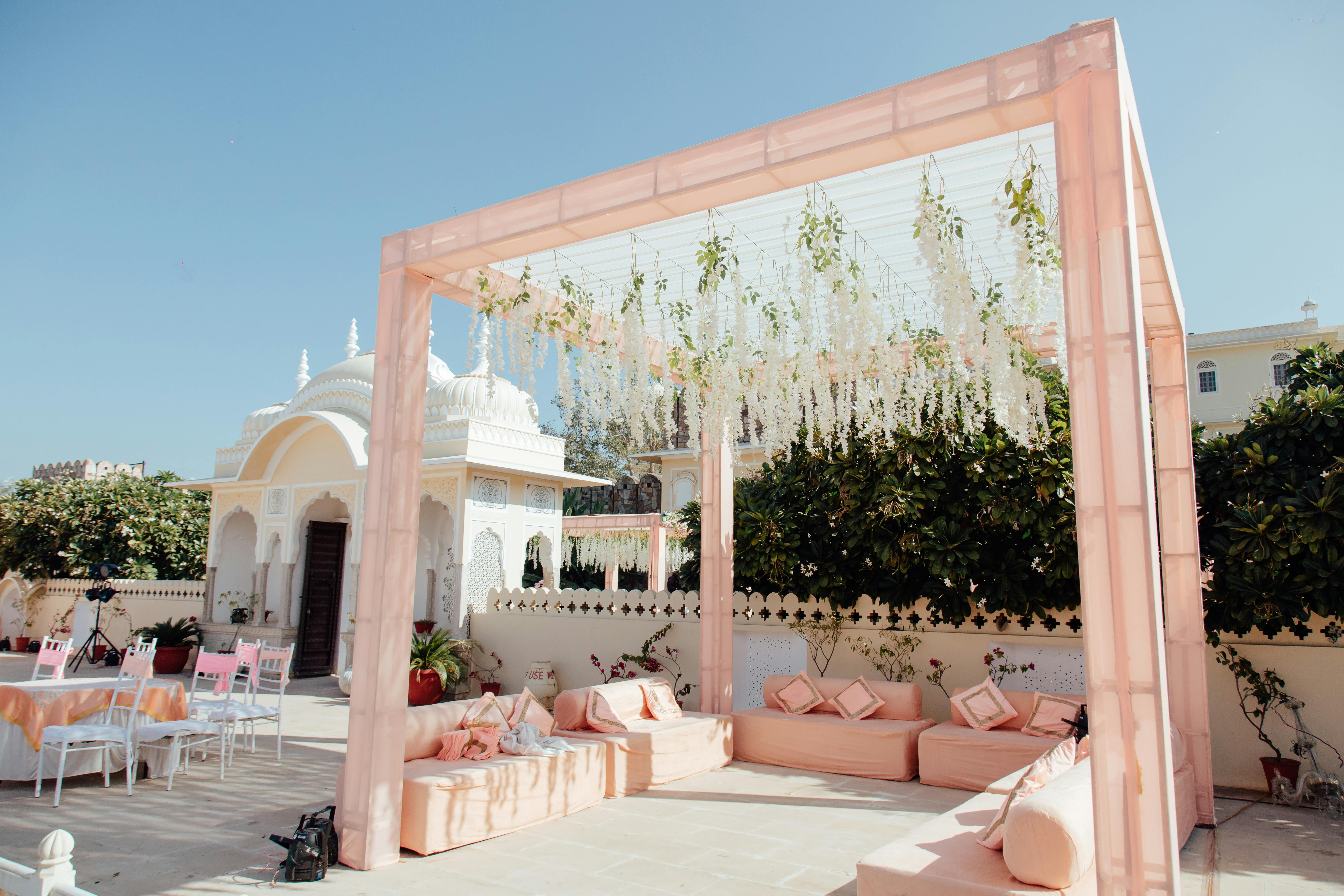 Luxurious outdoor wedding setup with floral decorations, pink seating, and elegant gazebo under a blue sky.