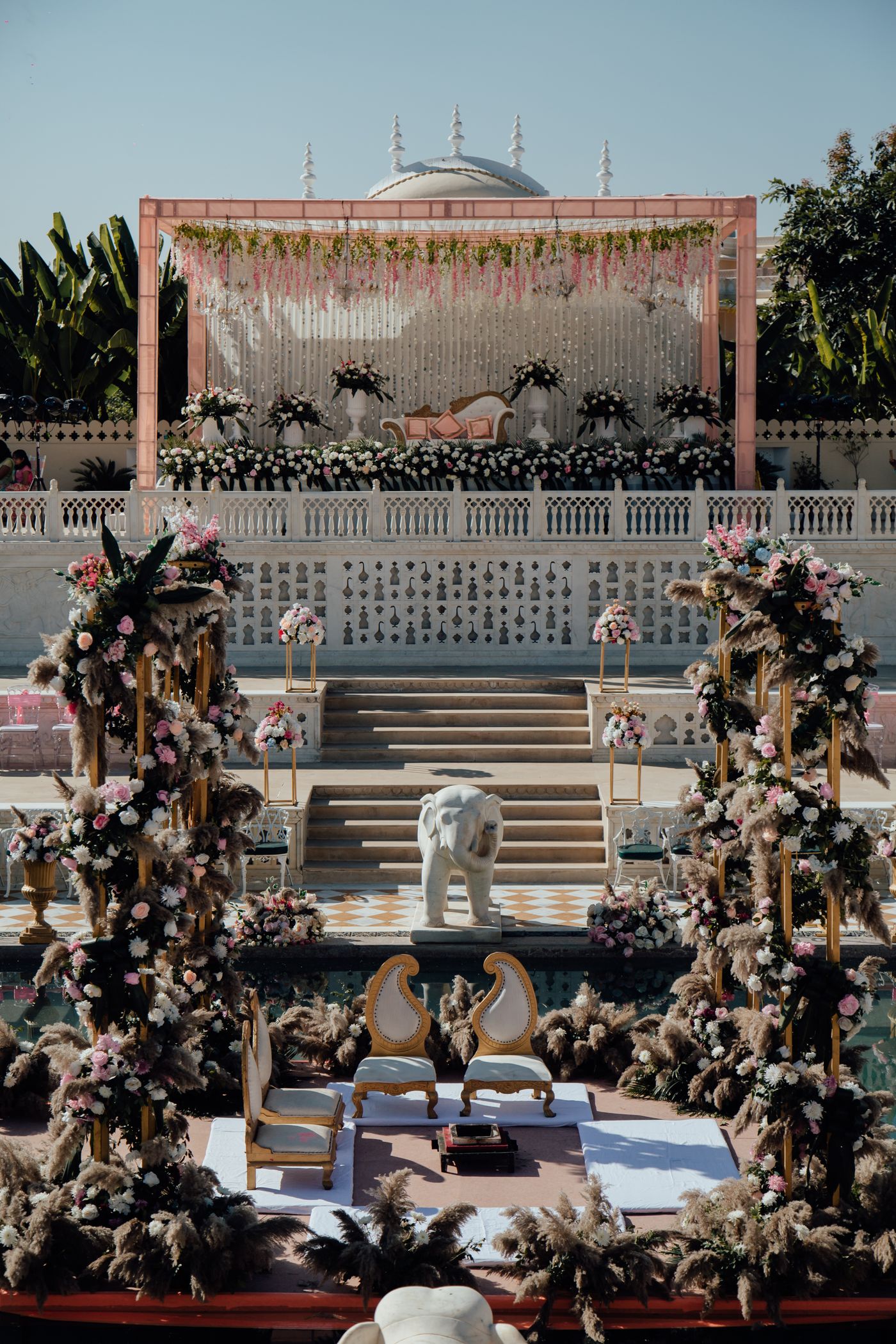 Blush pampas-and-rose mandap set beside a palace pool — representative image