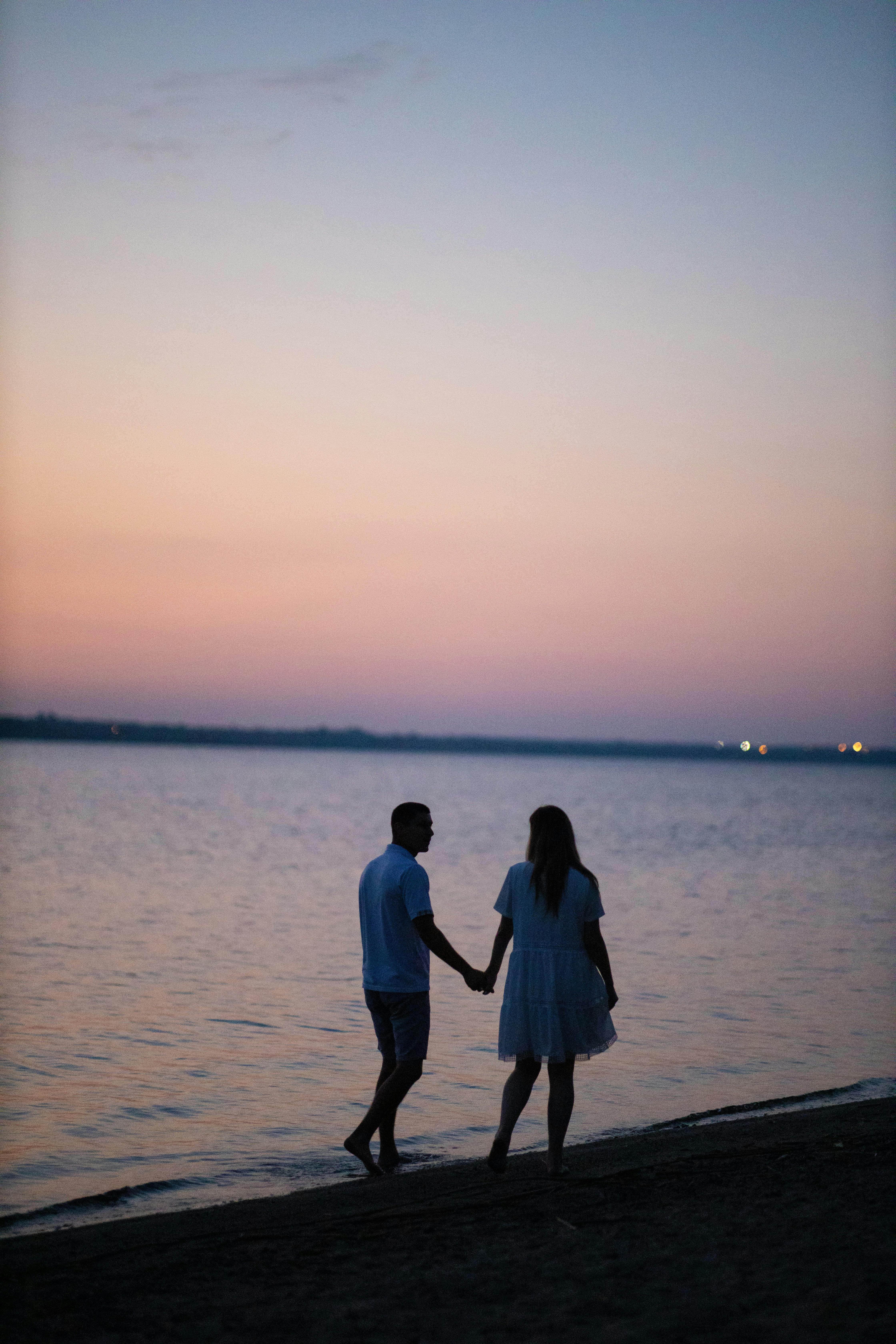 Silhouette of couple holding hands on the beach at sunset.