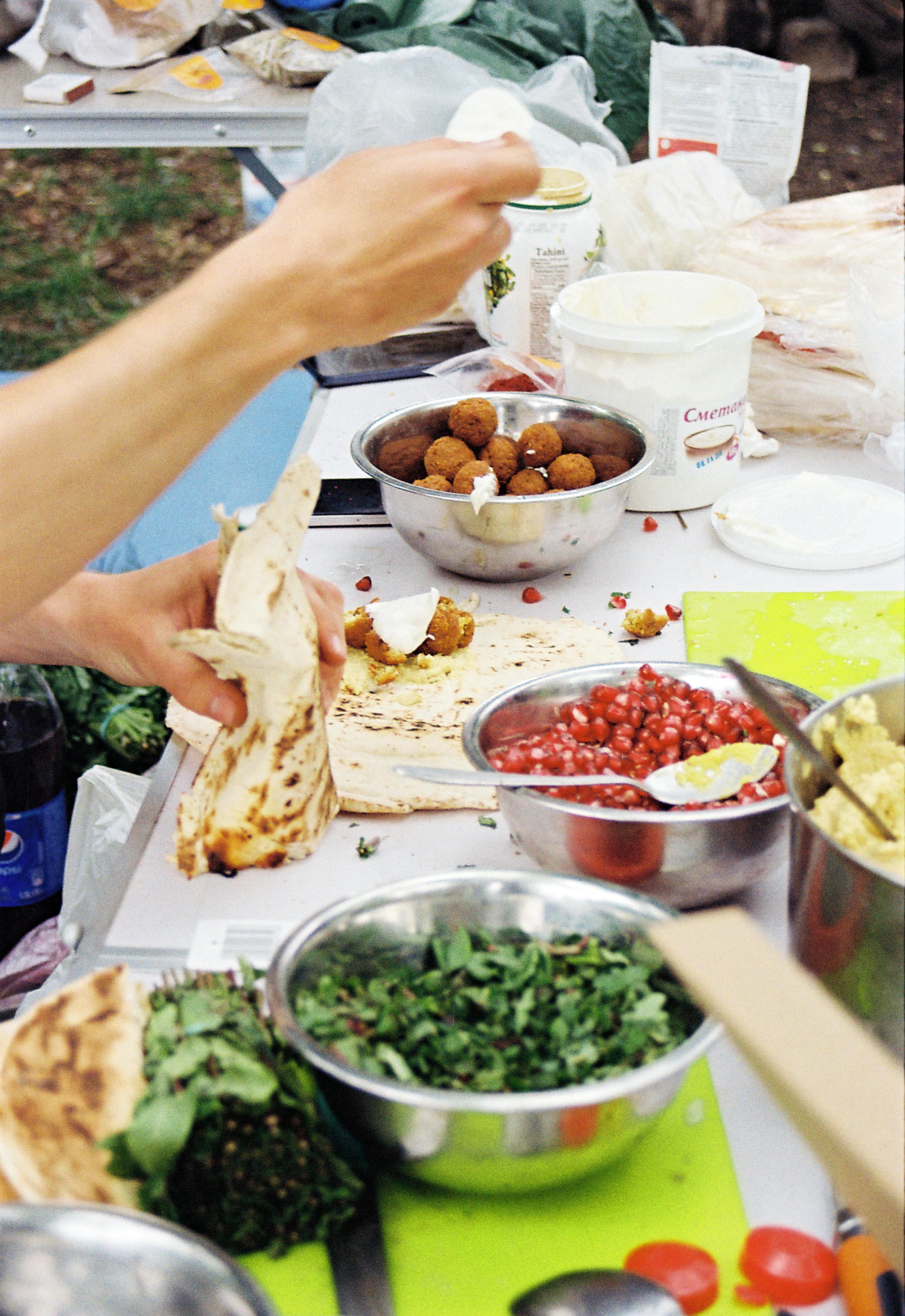 Colorful outdoor setup of preparing fresh falafel wraps with vibrant ingredients like herbs and pomegranate seeds.