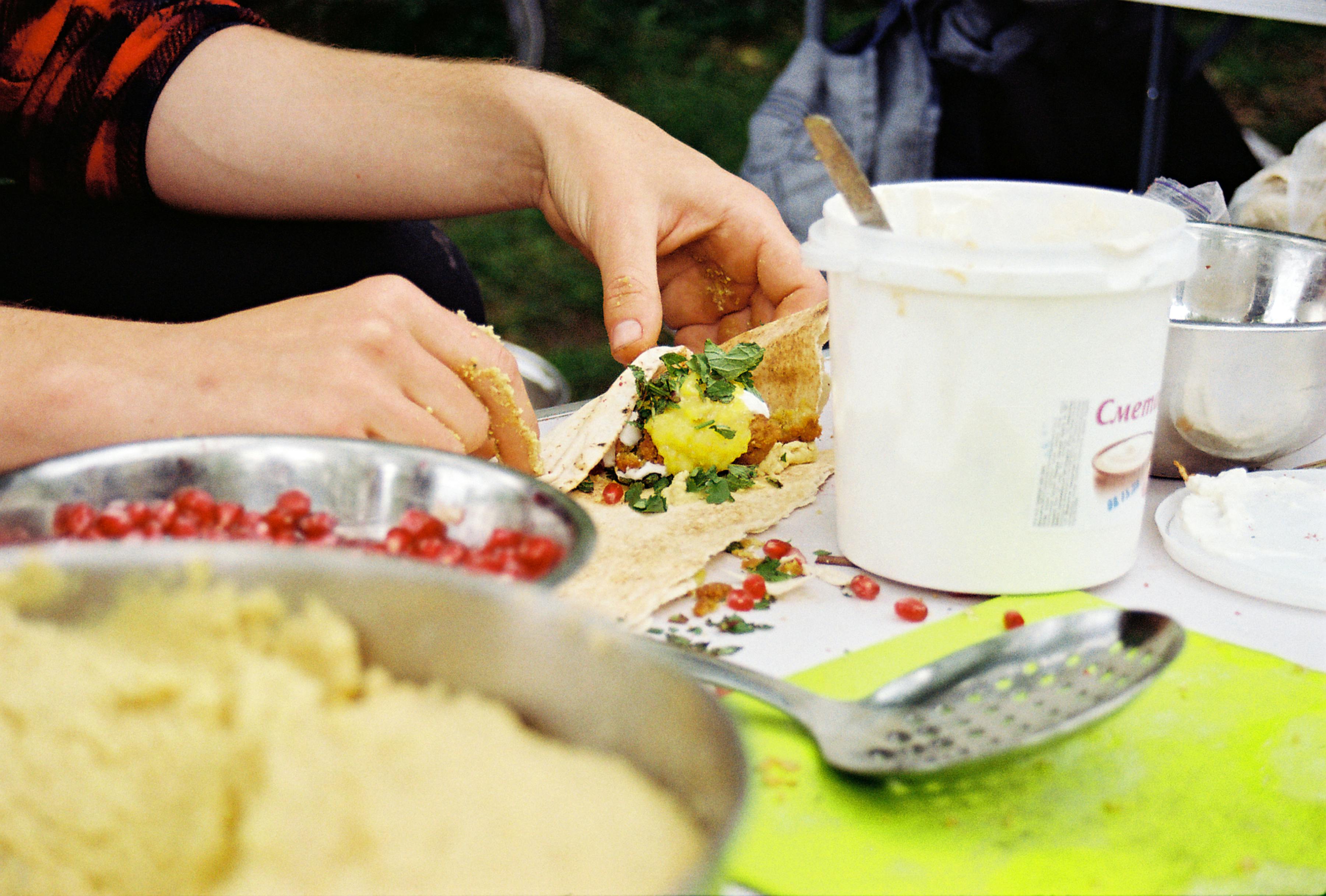 Close-up of hands making a fresh falafel wrap with herbs and pomegranate seeds, showcasing healthy ingredients.