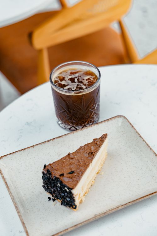 Free Tasty cheesecake slice with a refreshing glass of iced coffee in a cozy café setting. Stock Photo